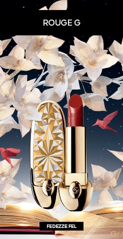 Guerlain Rouge G luxus rúzs arany mintás tokban, papírvirág dekorációval és elegáns csillagos háttérrel.